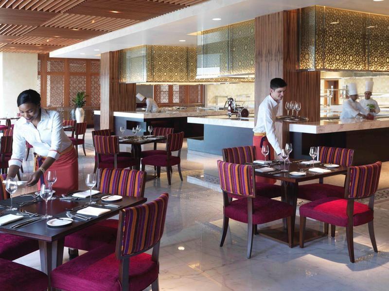 Modernes Restaurant mit rot bezogenen Stühlen, weißen Tischen und Kellnern in hellem Ambiente.