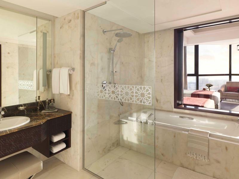 Helles Badezimmer mit Marmorboden, Duschecke, Badewanne, großem Spiegel und Fenster zum Wohnzimmer.