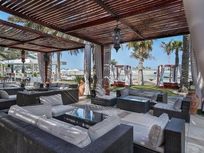 Terrasse couverte avec des sièges en osier confortables et vue sur les palmiers et la mer.