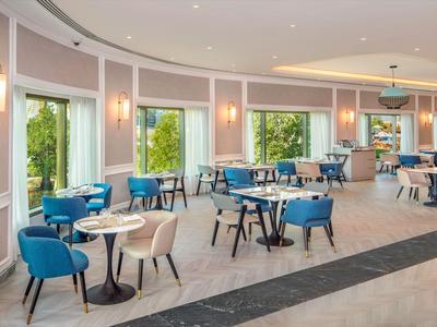 Restaurant moderne et lumineux avec des chaises bleues et de grandes fenêtres donnant sur la verdure.