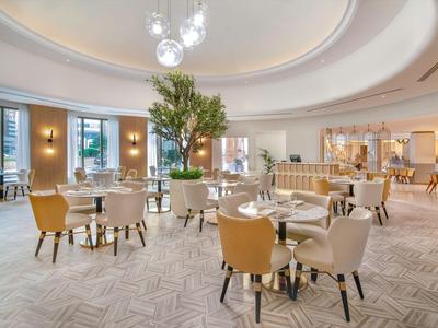 Espace lounge d'hôtel lumineux avec fauteuils confortables et plante centrale.