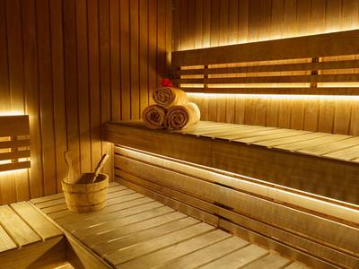 Sauna en bois avec bancs éclairés, serviettes et un seau de sauna avec louche.