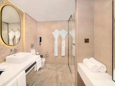 Elegant hotel bathroom with oval mirror, double sinks, and walk-in shower.