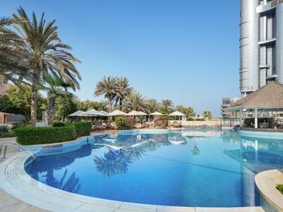 Grand piscine avec palmiers, parasols et bâtiment d'hôtel sous un ciel clair