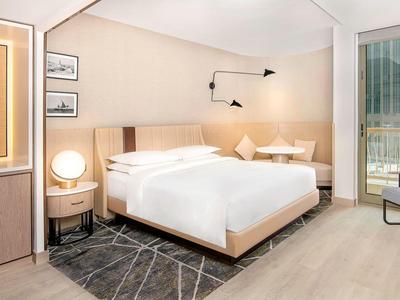 Modern hotel room with large bed, desk, chairs, and balcony with city view.