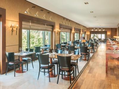 Restaurante luminoso con suelo de madera, mesas y sillas, grandes ventanas y diseño moderno.