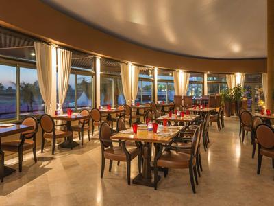 Elegant hotel restaurant with wooden chairs and tables, large windows, and sunset view.