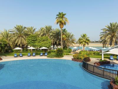 Piscina rotonda dell'hotel con palme, lettini e ombrelloni sotto un cielo limpido.