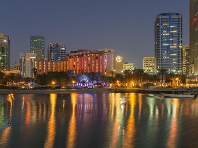 Horizonte nocturno de la ciudad con edificios iluminados y reflejos en el agua.