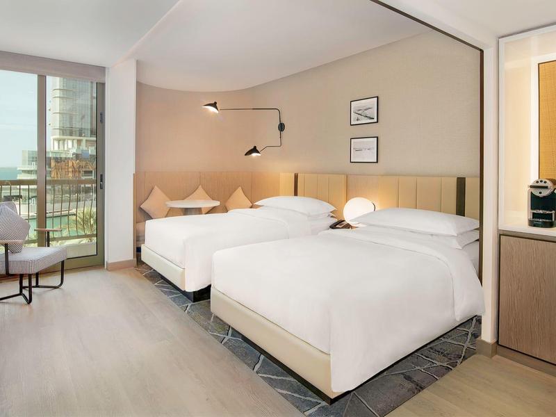 Brightly furnished hotel room with two double beds, balcony, and modern design.