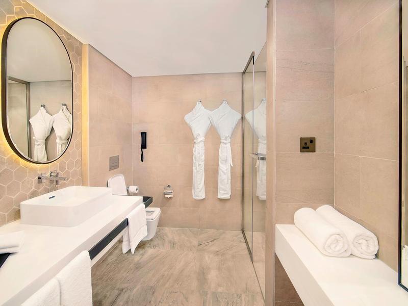 Elegant hotel bathroom with oval mirror, double sinks, and walk-in shower.