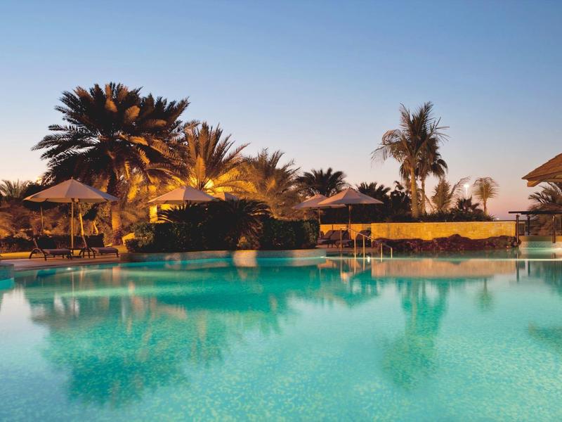 Evening hotel pool with illuminated palm trees and lounge area under clear sky.