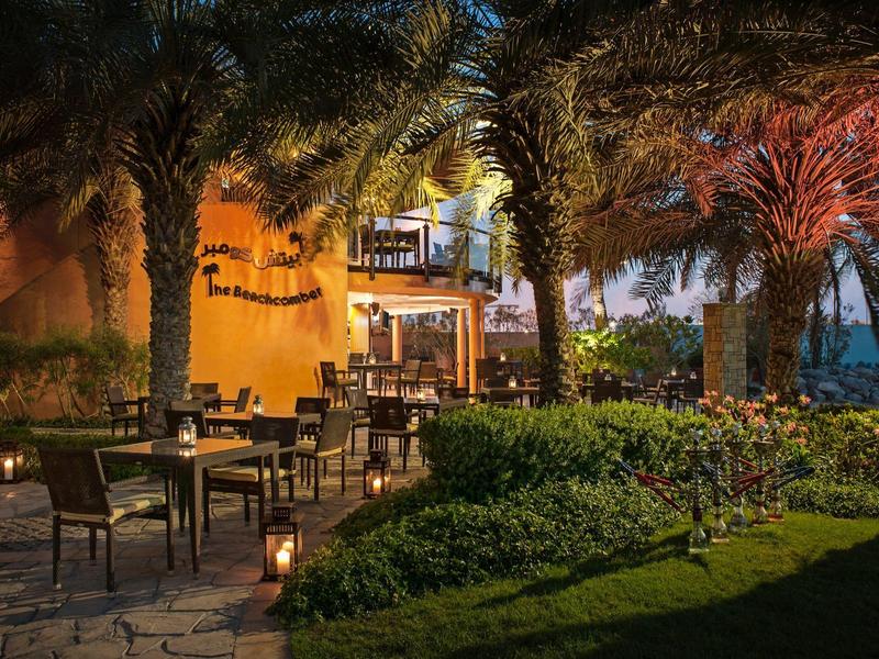 Cozy outdoor lounge next to a hotel with palm trees and soft lighting at night.