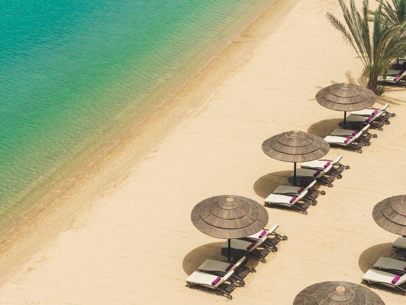 Beach with rows of sun loungers and umbrellas by clear sea.