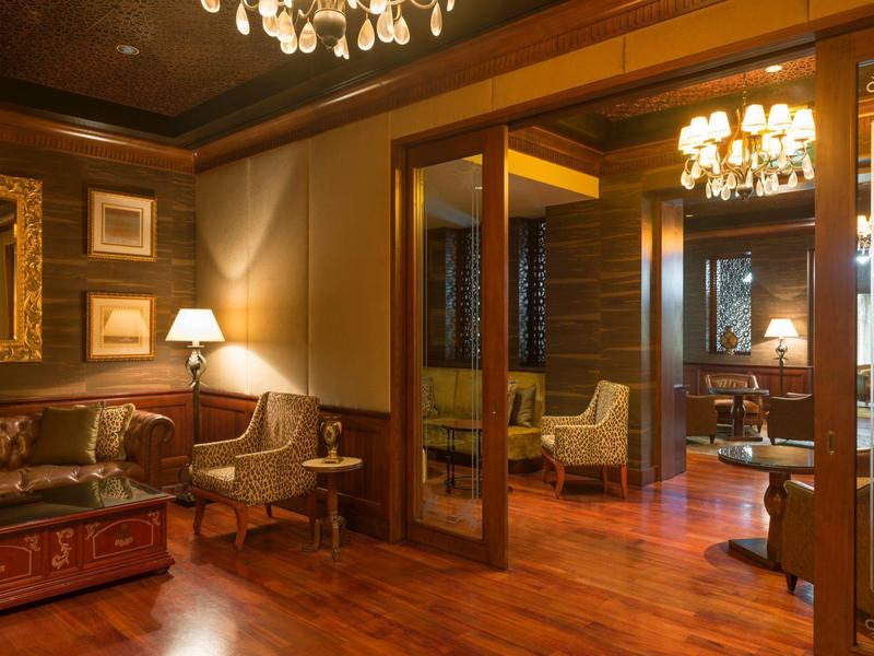 Elegant hotel room with wooden floors, leather sofa, armchairs, and warm lighting.