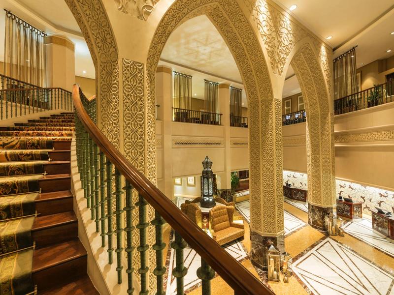 Luxurious hotel lobby with ornate arches, staircase, and oriental decor.