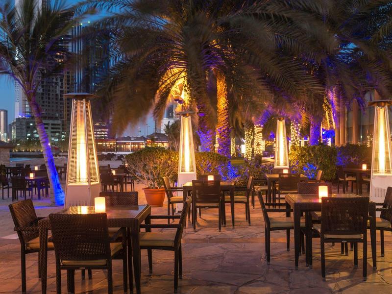 Evening terrace with tables, chairs, and heaters under palm trees