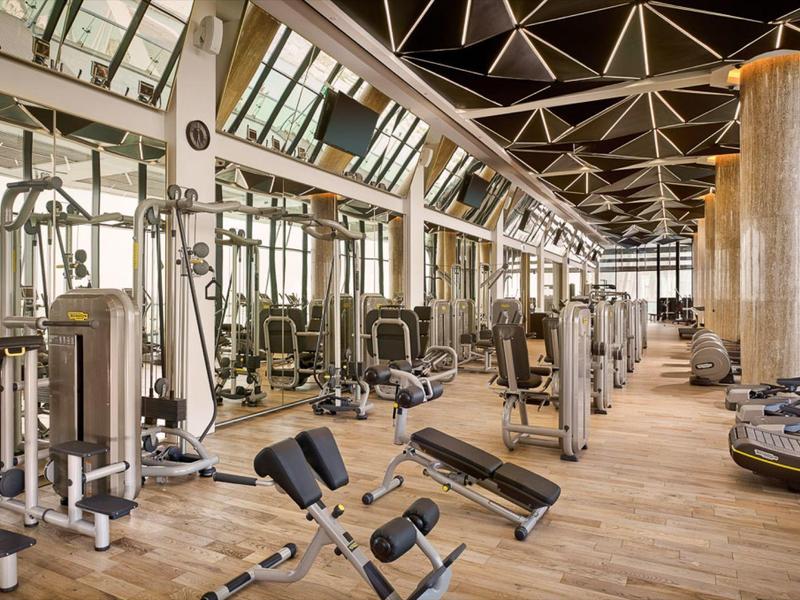 Grote fitnessruimte met moderne apparatuur en houten vloer in een hotel.