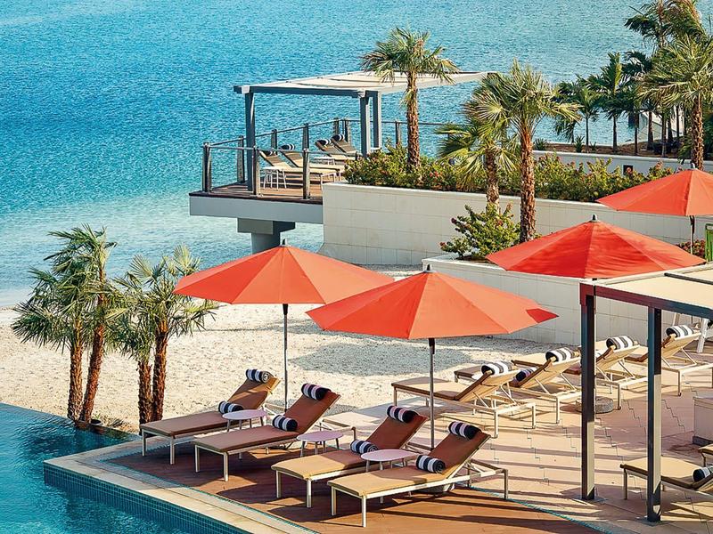 Luxe zwembadgedeelte met ligstoelen en oranje parasols naast zeezicht.