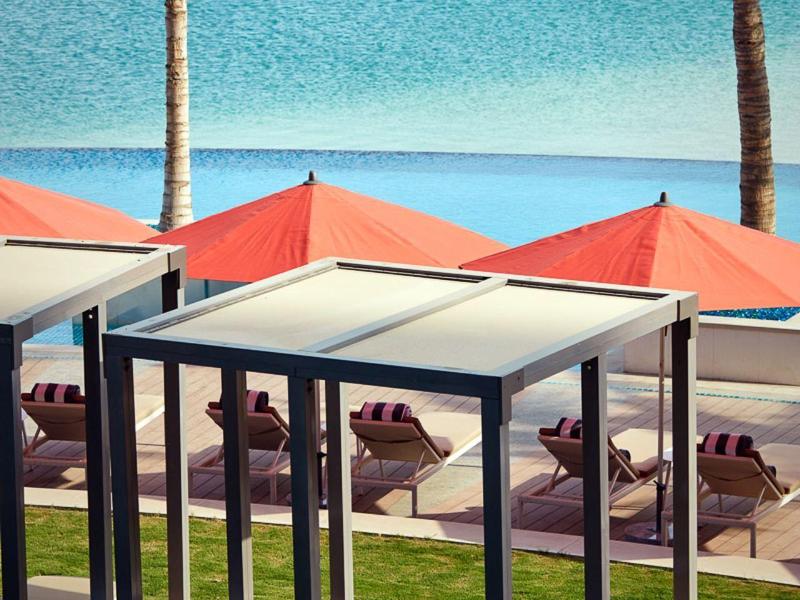 Hotel zwembad met ligstoelen, rode parasols en palmbomen bij zee