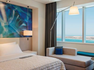 Hotelzimmer mit Doppelbett, moderner Kunst an der Wand und Meerblick durch großes Fenster.