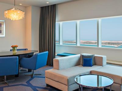 Modern eingerichtetes Hotelzimmer mit Sofa, Esstisch und großer Fensterfront mit Meerblick.