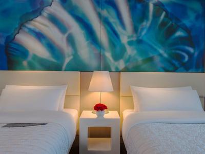 Modernes Hotelzimmer mit zwei Einzelbetten, Nachttisch und blauem abstraktem Kunstwerk an der Wand.