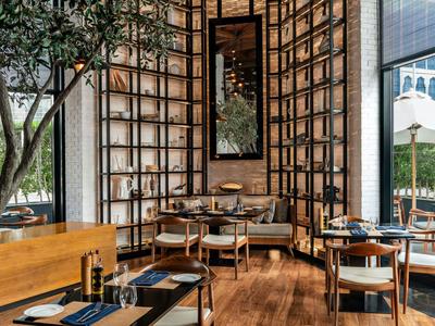 Modernes Restaurant mit Holzstühlen und Tischen, großer Fensterfront und grünem Baum im Innenbereich.