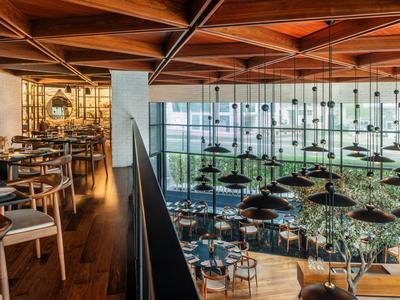 Modernes Restaurant mit Holzdecke, großen Fenstern und eleganten Tischen und Stühlen in hellem Licht.