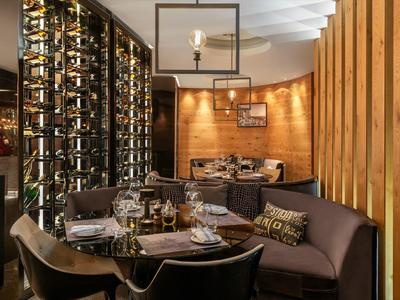 Gemütliches Restaurant mit runden Tischen, Holzwänden und einem großen Weinregal.