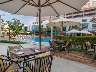 Poolbereich mit Sitzgelegenheiten und Sonnenschirmen in einem Hotelgarten.