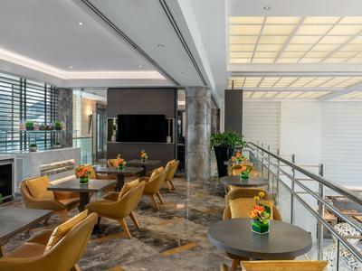 Moderner, heller Loungebereich mit bequemen Stühlen, Tischen und großen Fenstern an der Seite.