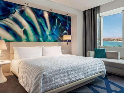 Modernes Hotelzimmer mit großem Bett, abstraktem Wandbild und Blick auf das Meer.