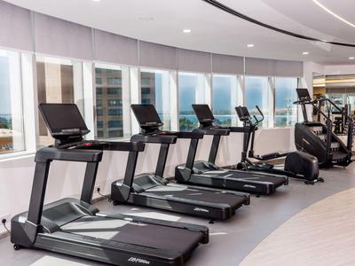 Moderne Fitnessgeräte in einem hellen Fitnessraum mit großen Fenstern und Blick auf die Stadt.