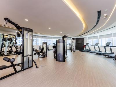 Světla, moderní posilovna s cvičebními stroji a běžeckými pásy u velkých oken.