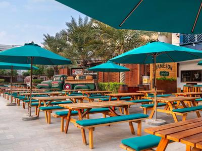 Outdoor-Biergarten mit Holztischen und grünen Sonnenschirmen neben einem Restaurant.