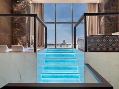 Modernes Hotelzimmer mit leuchtender Treppe und Panoramafenster mit Stadtblick.