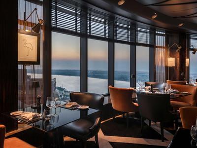 Elegantní hotelová restaurace s velkými okny s výhledem na vodu při západu slunce.