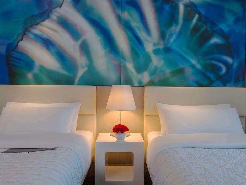 Modernes Hotelzimmer mit zwei Einzelbetten, Nachttisch und blauem abstraktem Kunstwerk an der Wand.