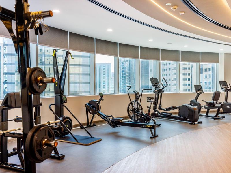 Moderne Fitnessstudio mit Geräten wie Rudergerät, Laufband, Crosstrainer und Kraftstation vor großen Fenstern.