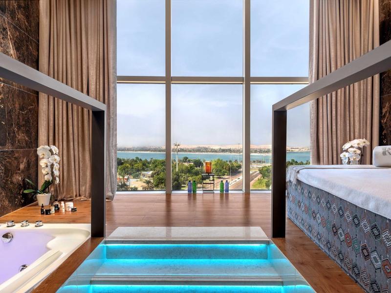 Modernes Bad mit großer Glasfront, freistehender Badewanne und hellblau beleuchtetem Treppenaufgang.