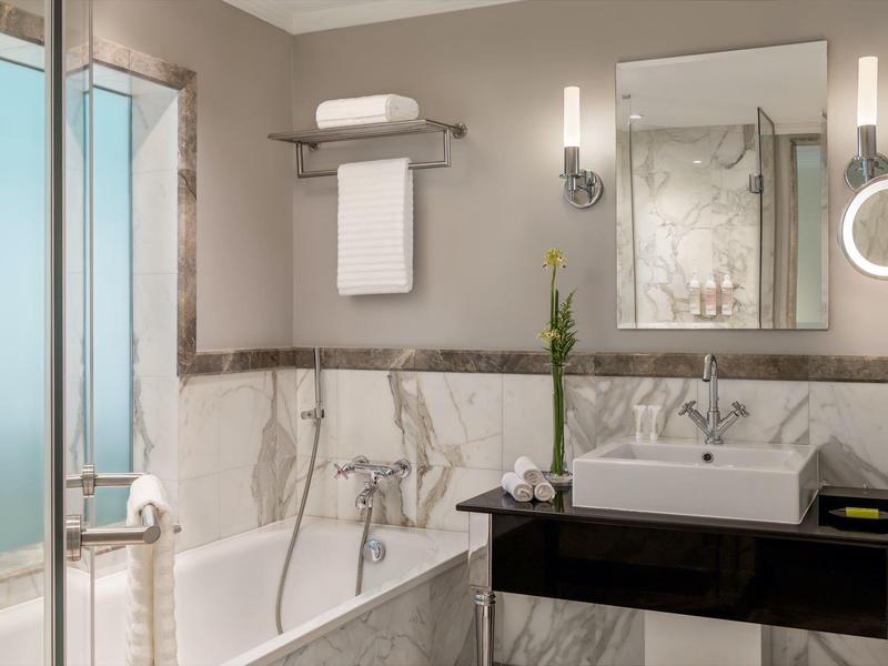 Elegantes Badezimmer mit Badewanne, Waschbecken auf schwarzem Podest und großem Spiegel.