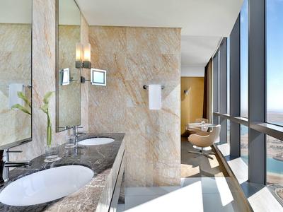 Helles Hotelbadezimmer mit Marmorwaschbecken, großer Spiegelwand und Panoramafenstern mit Meerblick.