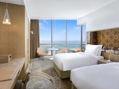 Modernes Hotelzimmer mit zwei Betten, großem Fenster und Meerblick.