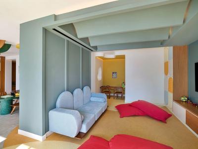 Área moderna de habitación de hotel con sofá azul, cojines rojos y diseño minimalista.