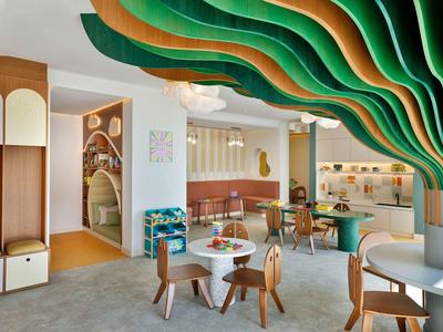 Sala común moderna de hotel con acentos ondulados y coloridos en el techo y áreas de descanso.