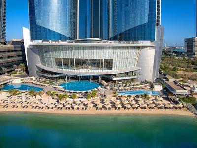 Luxushotel mit Pool, Strandliegen und klarem Meer an sonnigem Tag