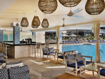 Moderner Poolbereich mit Bar, geflochtenen Lampen und gemütlichen Sitzmöbeln in hellem Ambiente.