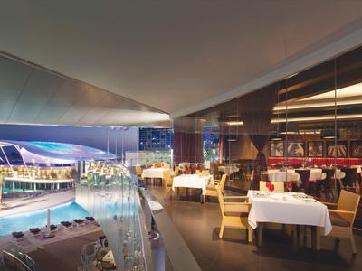 Elegante restaurante con mesas vestidas y vista a una piscina iluminada al anochecer.