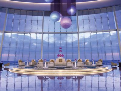 Amplio vestíbulo moderno con recepción circular y grandes ventanales con vistas al cielo y al mar.